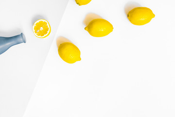Water bottle and a few lemons on pastel grey and white background. Flat lay, top view