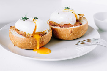 Poached eggs on a bun with bacon on a plate close up