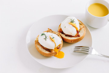 Poached eggs on a bun with bacon on a plate with orange juice