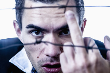 Fuck the system and freedom concept. Man behind a barbed wire shows a middle finger gestureю