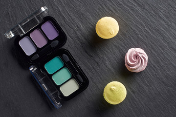 Eye shadows palettes with macarons and meringue on dark slate background