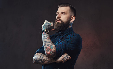 Pensive handsome old-fashioned hipster in a blue shirt and suspenders, standing with hand on chin...