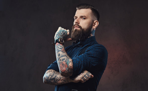 Pensive handsome old-fashioned hipster in a blue shirt and suspenders, standing with hand on chin in a studio.
