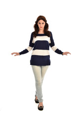 full length portrait of girl wearing striped blue and white jumper and jeans. standing pose on white studio background