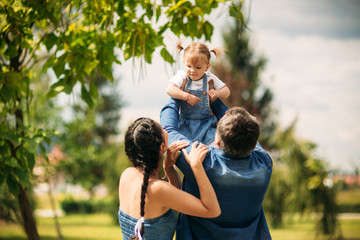 Happy joyful young family father, mother and little daughter having fun outdoors, playing together in summer park, countryside. Mom, Dad and kid laughing and hugging, enjoying nature outside