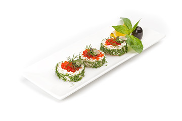 The rice medallions with red caviar and sauce, with a segment of a lemon and olives, decorated with fresh leaves of the pepper mint. The dish is isolated on a white background.