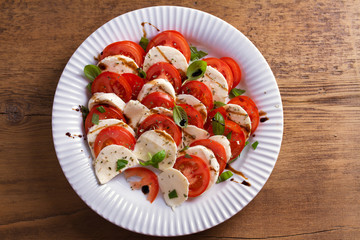 Italian caprese salad with sliced tomatoes, mozzarella cheese, basil, olive oil and balsamic vinegar. View from above, top studio shot