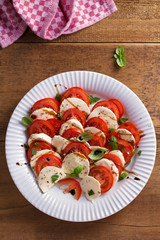 Italian caprese salad with sliced tomatoes, mozzarella cheese, basil, olive oil and balsamic vinegar. View from above, top studio shot