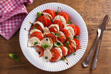 Italian caprese salad with sliced tomatoes, mozzarella cheese, basil, olive oil and balsamic vinegar. View from above, top studio shot