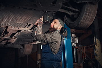 Fototapeta na wymiar Auto mechanic in a uniform, repair the car with a screwdriver while standing under lifting car in the repair garage. 