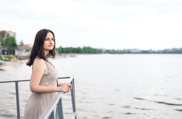Fototapeta na wymiar Young woman walks along waterfront. Brunette woman in gray summer dress