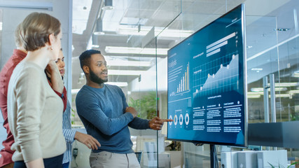 Diverse Team of Young Professionals in Conference Room Have Discussion about Statistics and Graphs Shown on a Presentation TV.
