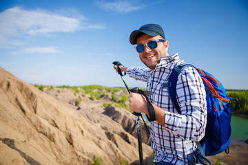 Photo of cheerful tourist man with backpack stretching forward with sticks for walking on hill
