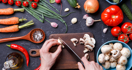 Picture on top of fresh vegetables, mushrooms, cutting board, oil, knife, hands of cook