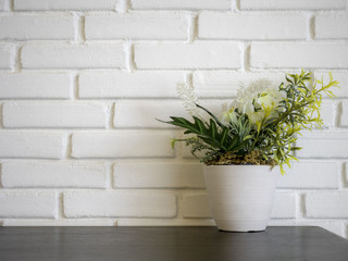 Front view of plant and flower mock-up in white flowerpot on wooden desk in front of white brick wall texture background, Copy space