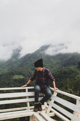 Asian young man in Scottish shirt and black hat sitting at mountain peak with clouds and fog outdoor hiker. Doi Luang Chiang Dao Chiang Mai, In morning.