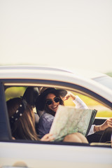 Two young women having fun on road trip,checking map.