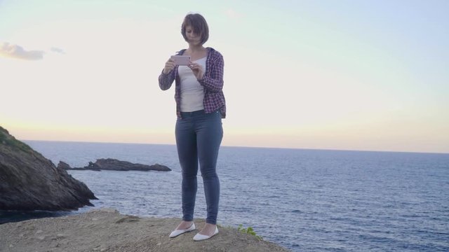 Young woman standing on top of a mountain takes pictures sea. Sunset