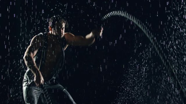 Athletic man working out with battle ropes in the rain. Slow Motion.