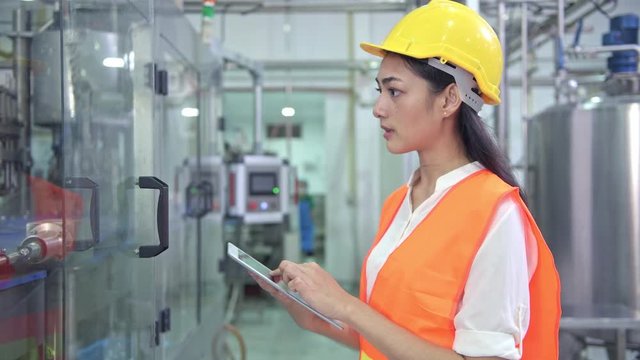 Woman industrial engineer at work in factory. Beautiful young chinese engineer working in large factory. With safety helmet and jacket. High tech automatic machine in background.