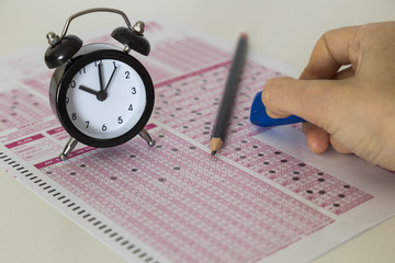 optical form and student selection and placement test,clock,glasses,pen,hand on the table.Stress of University exam.