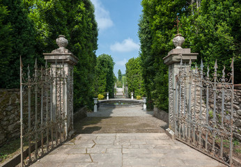 Fototapeta na wymiar A glimps of the park of Villa Reale in Marlia, Lucca. An old iron gate opens to the formal garden.