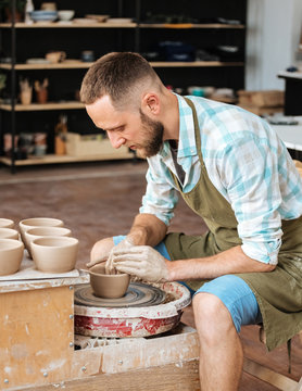 Man is  shaping bowl on potters wheel.
