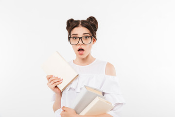 Photo of excited teenage girl 20s with double buns hairstyle and dental braces expressing puzzlement while holding many studying books, isolated over white background