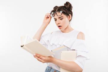 Photo of european concentrated educated girl 20s having double buns hairstyle and dental braces studying and reading books with interest, isolated over white wall