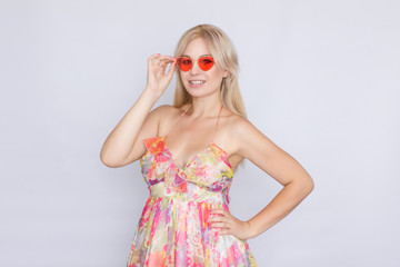 portrait of a young blond woman with long hair in a floral pink dress, and bright pink sunglasses