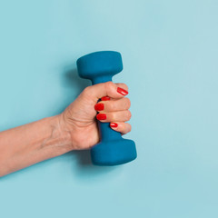 Female hand holding blue dumbbell on blue pastel background. Sport concept.