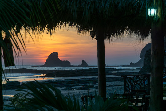 Colorful sunset on the beach in Nicaragua with a rock and banana leafes in the front.