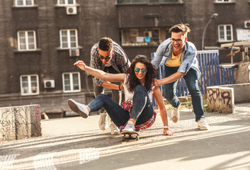 Group of friends hangout at the city street.Female sitting on skate board while friends pushing her...