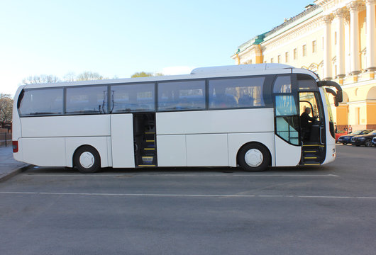 White Modern Tourist Coach Bus on Parking Lot of City Street. Simple Empty Bus on Asphalt Road on Summer Day. Travel and Tourism Concept, Regular Transportation for Tourists on Sightseeing Tour.