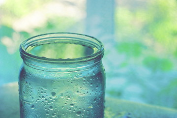 a water drop jar with water on the glass.  a can full of water by the window.