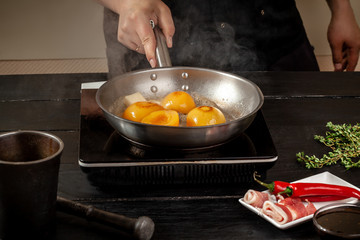 Peaches on a fry pan. Canned fruit yellow peaches, black wooden background, board.