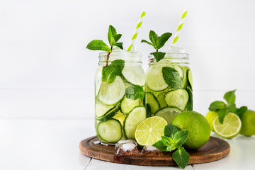 Two jars of fruit and herb infused water with cucumber, lime and mint and ice cubes on white background. The concept of detox and weight loss. Copy space