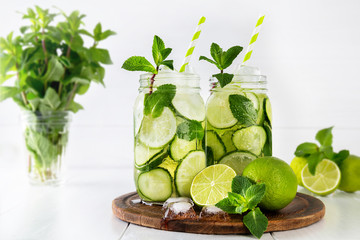 Two jars of fruit and herb infused water with cucumber, lime and mint and ice cubes on white background. The concept of detox and weight loss.