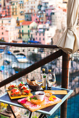 Romantic dinner for two at sunset. White wine and Tasty italian snack: fresh bruschettes  and meat on the board in outdoor cafe with amazing view in Manarola