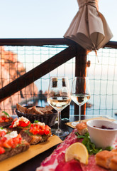 Romantic dinner for two at sunset. White wine and Tasty italian snack: fresh bruschettes  and meat on the board in outdoor cafe with amazing view in Manarola