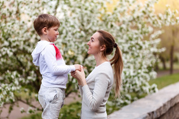 beautiful young mom holding hands with little son outdoors