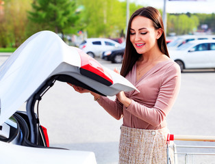 Young pretty woman is opening the trunk of her car © Nobilior