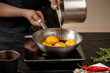 Peaches on a fry pan. Canned fruit yellow peaches, black wooden background, board.
