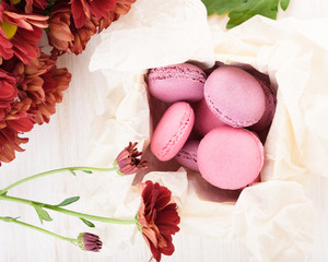 French macaroons in a box. Sweet cakes and a red chrysanthemum flowers on a wooden table. Copy space, flat lay