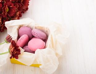 French macaroons in a box. Sweet cakes and a red chrysanthemum flowers on a wooden table. Copy space, flat lay