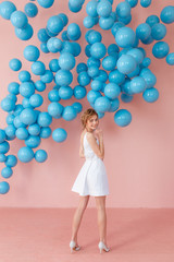 Fototapeta premium Back view of beautiful young woman standing over pink background and blue balls