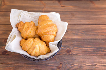 Three croissants in basket on wooden brown table