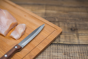 Piece of raw chicken meat cut with knife on wooden table