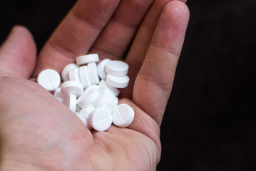White pills in hand on black background closeup