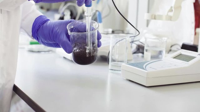 Close up hands of a scientist in the laboratory measuring pH of the sample suspension by electronic pH meter